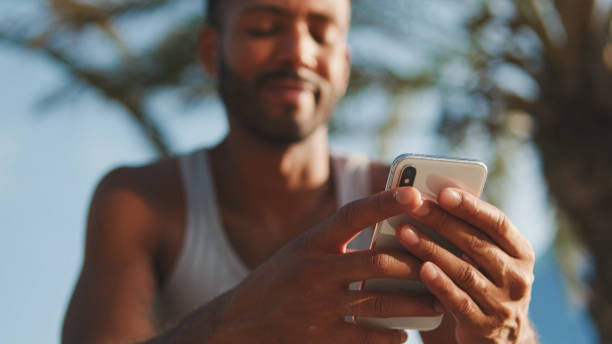 istock Young bearded male athlete is resting after training, sitting on bench, using smartphone 1455304735