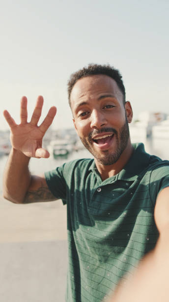 istock Happy young man making video call from phone while sitting in harbor with yachts on background 1455304832
