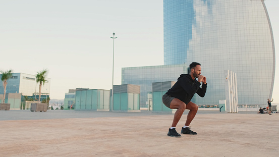Young bearded male athlete doing workout, squats and jumping on the waterfront