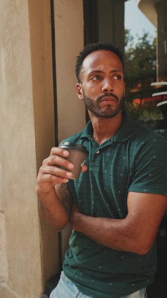istock Young man drinking coffee while sitting in street cafe on cityscape background 1455304867