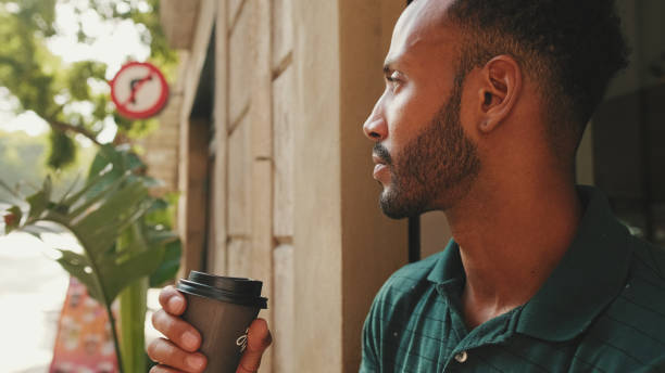 istock Young man drinking coffee while sitting in street cafe on cityscape background 1455304896