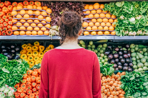 Rear view of a woman shopping for healthy food in grocery store. Young female customer looking at the produce section in a supermarket.