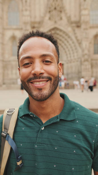 istock Close-up of young tourist man with backpack on his shoulder, looking at the camera while standing on the square of the old city 1455305251