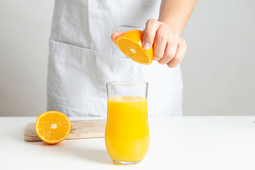 Unrecognizable caucasian female is squeezing orange juice into a drinking glass on a white table.