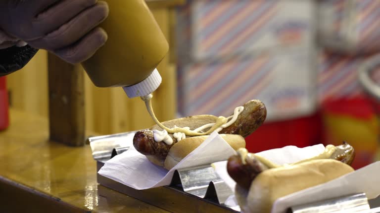 Unrecognizable person pouring mayonnaise on a sausage in a bun, on the Christmas market stand