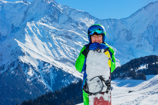 Portrait of a young 11 years old happy boy with snowboard in the mountains peaks of French Alps