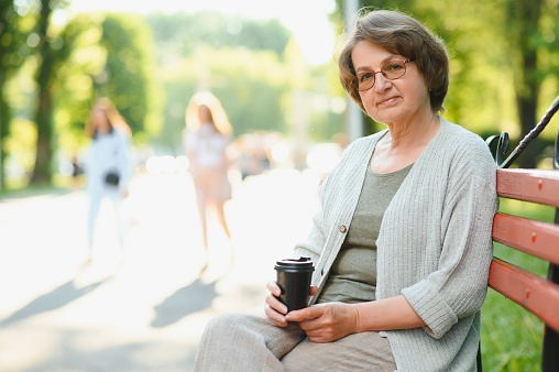 Portrait of aged positive peaceful lady sitting bench hold coffee.