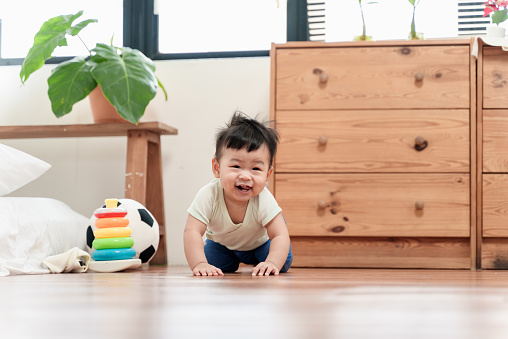 Portrait of cute Asian baby boy crawling on the floor at home, smiling and looking at camera. Asian family baby domestic life concept.