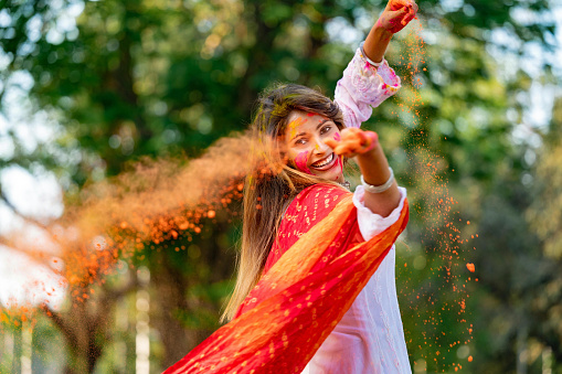 Happy young beautiful girl playing with colours on the occasion of Holi festival at an outdoor park. Holi also known as festival of colours , a popular Hindu festival celebrated across India.
