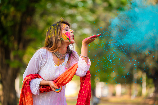 A beautiful young girl blowing colorful powder on Holi festival. Holi is a popular ancient Hindu festival, originating from the Indian subcontinent. It is celebrated predominantly in India and Nepal.