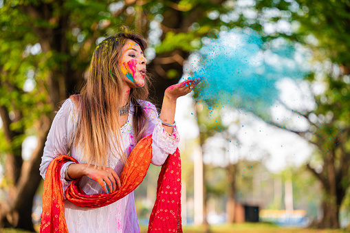 A beautiful young girl blowing colorful powder on Holi festival. Holi is a popular ancient Hindu festival, originating from the Indian subcontinent. It is celebrated predominantly in India and Nepal.