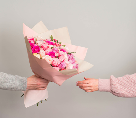 Man hand giving roses flowers bouquet to woman on grey background. Valentines or mothers day concept.