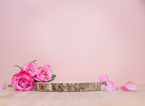 Wooden podium or product stage with pink roses on pastel background.