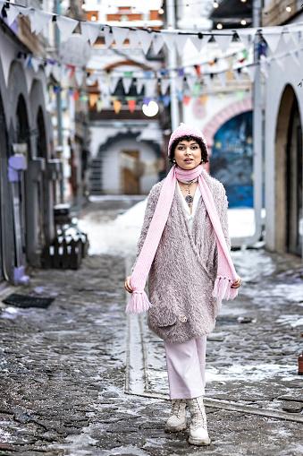 Portrait of a smiling stylish young woman in pastel-colored warm clothes outdoors in the city in winter.Snowfall,cold weather.