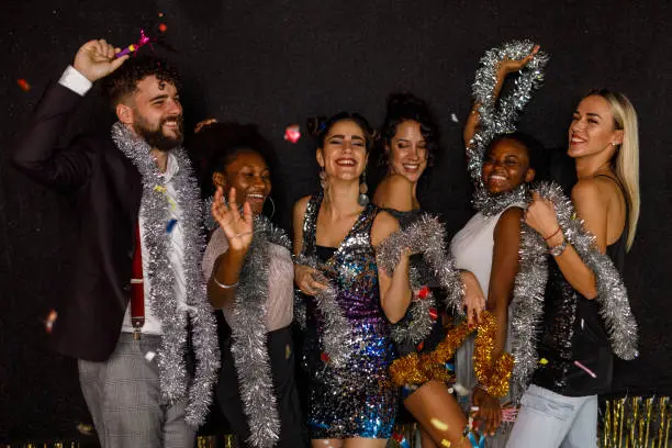 Photo of Cheerful group of friends dancing during a New Year's countdown while colorful confetti are falling down