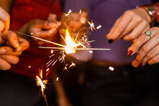 Close up shot of unrecognizable group of friends holding their sparklers together while igniting them during a fun New Year's eve party.