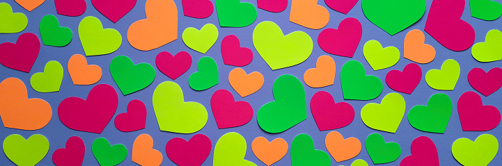 Pink, yellow, orange and green paper hearts on a bright blue background. Top view. Theme of love.