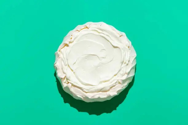 Above view with a homemade pavlova cake, minimalist on a green table. Australian traditional dessert, crispy meringue crust filled with whipped cream