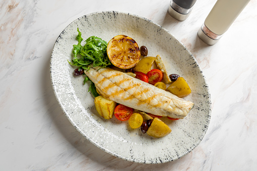 sea bass fillet with grilled vegetables and lemon on marble table top view