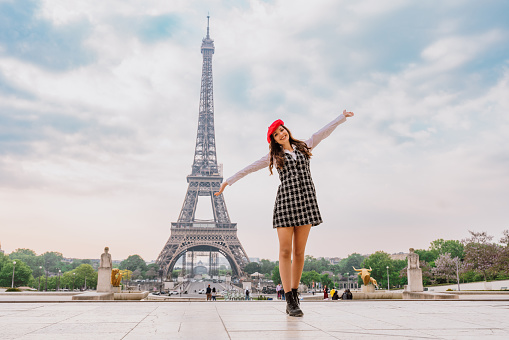 Beautiful young woman visiting paris and the eiffel tower. Parisian girl with red hat and fashionable clothes having fun in the city center and landmarks area