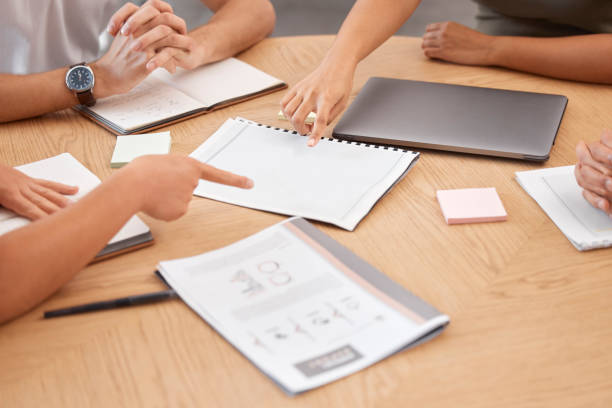 istock Documents, paperwork and pointing hands in business meeting with papers on desk. Teamwork, collaboration and business people in discussion, planning and working on strategy, analytics and project 1455326457