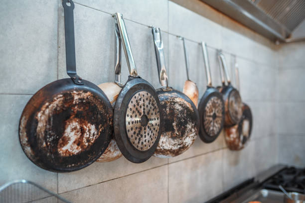 Indoor shot of a kitchen. Cooking equipment hanging on the wall. Multiple frying pans with different dimensions.