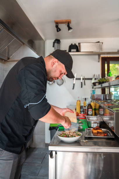 istock Side Shot of Male Chef Adding Cheese to a Cesar Salad 1455326575