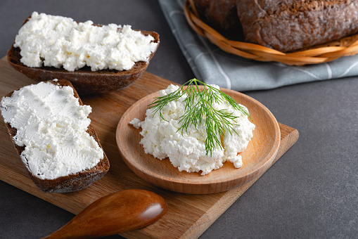 Home made rye bread on a wooden cutting board with curd cheese, ricotta and dill.