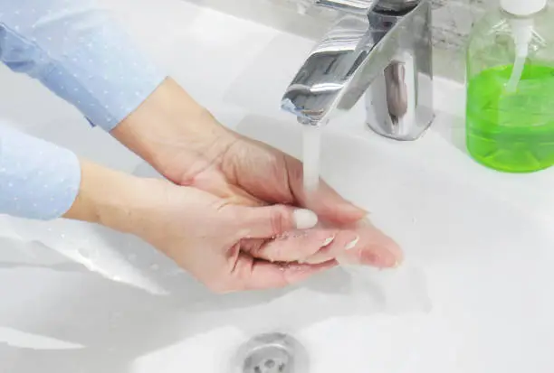Photo of hand washing with soap or gel under running water in the washbasin, cleanliness and hygiene, woman's hands dressed in blue shirt