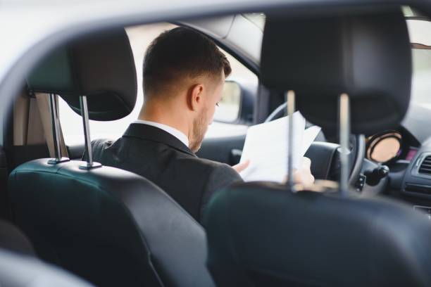 istock Always in a hurry. Handsome young man in full suit smiling while driving a car. 1455329556
