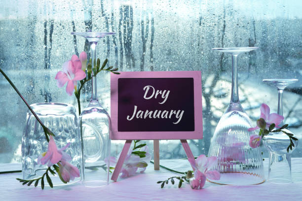 Dry January, month without alcohol. Text Dry January on blackboard, chalk board. Empty vine and beer drinking glasses, freesia flowers. Window with raindrops, grey winter city skyline behind. stock photo