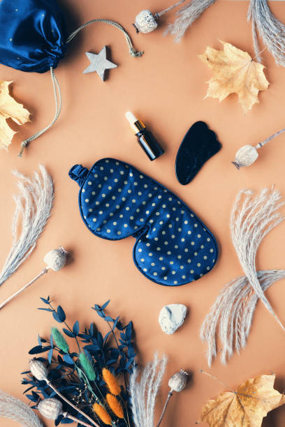 istock Sleeping mask, gua sha stone, massage roller, essence serum, oil bottle. Face care, wellness therapy background. Healthy sleep, massage, natural meditation tools with eucalyptus and dry poppy plants. 1455332348