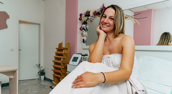 Portrait of a happy woman sitting in a spa, she's wearing a white towel, after her spa day