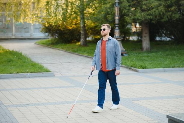 junger blinder mann mit weißem stock geht über die straße in der stadt - accessability stock-fotos und bilder