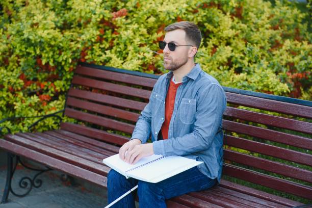 istock Blind man reading book on bench in park 1455338767