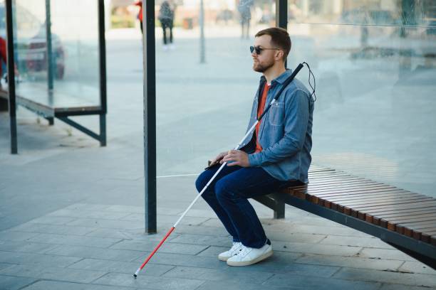 istock Visually impaired man with walking stick, sitting on bench in city park. Copy space 1455339299