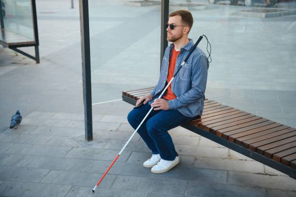 istock Visually impaired man with walking stick, sitting on bench in city park. Copy space 1455340496