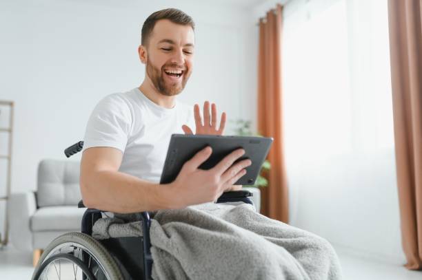istock Man in wheelchair using tablet computer at home. Positive retired male with physical disability browsing web on touch pad, watching video online indoors. 1455343269