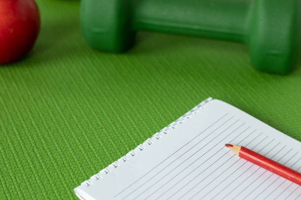 istock Blank notebook with pencil on green workout mat with red apple and dumbell in the background, a closeup 1455344657