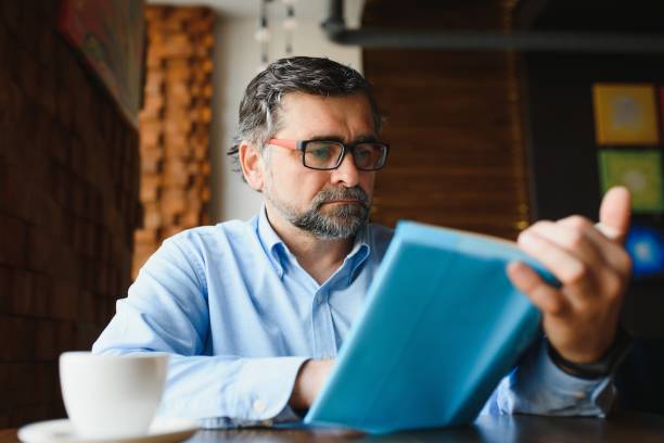 istock Mature handsome man reading a book in a cafe 1455347108