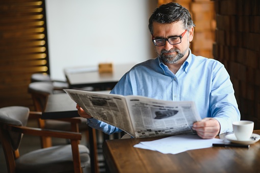 Businessman sitting on the couch and reading news on the financial newspaper, he is smiling at camera