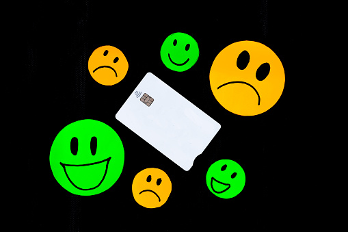 A white plastic card with a chip with contactless payment technology with some drawings of smiling and sad faces on a black background.