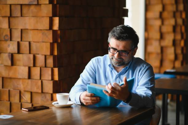istock Mature handsome man reading a book in a cafe 1455348707