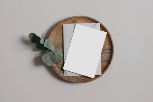 istock Blank greeting card, invitation and envelope mockup. Wooden plate, tray. Beige table background with dry eucalyptus leaves, branch. Moody wedding composition, office supply. Flatlay, top. No people. 1455349271