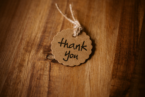 Thank you word written in a card on wooden background with selective focus. Love and gratitude concept.