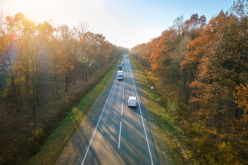 Aerial view of intercity road with fast driving cars between autumn forest trees at sunset. Top view from drone of highway traffic in evening.