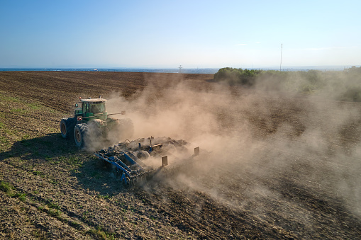 Aerial view of tractor plowing agriculural farm field preparing soil for seeding in summer.