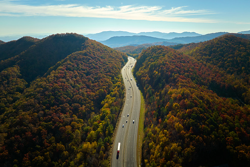 View from above of I-40 freeway in North Carolina heading to Asheville through Appalachian mountains in golden fall season with fast driving trucks and cars. Interstate transportation concept.