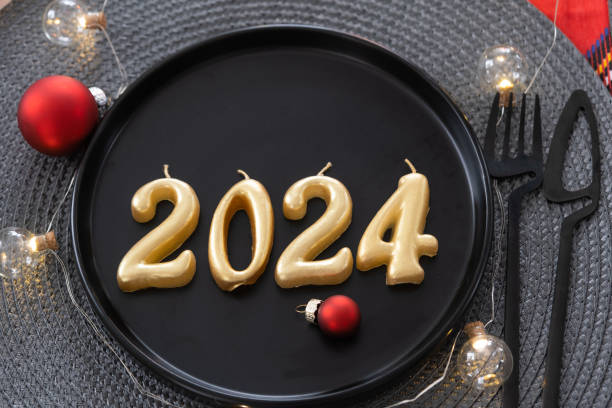 istock Golden figures 2024 from candles on a black plate on a festive table with a New Year's serving. Loft-style interior, party, feast. Wicker napkin, fork, knife 1455359049