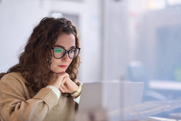 Young woman worker wearing glasses watching online webinar at work. Young serious busy professional business woman employee or student wearing glasses using laptop watching online webinar or training web course, looking at computer, thinking, doing research. insta stock pictures, royalty-free photos & images